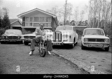 Elton John im Bild bei ihm zu Hause, sitzend auf einem kleinen Motorrad vor vier seiner Autos, darunter ein Mercedes (2. links) und ein weißer Rolls Royce (3. links).Foto vom 4.. April 1972 Stockfoto