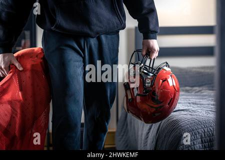 Ein junger Mann mit einem Fußballhelm in seinem Zimmer. Stockfoto