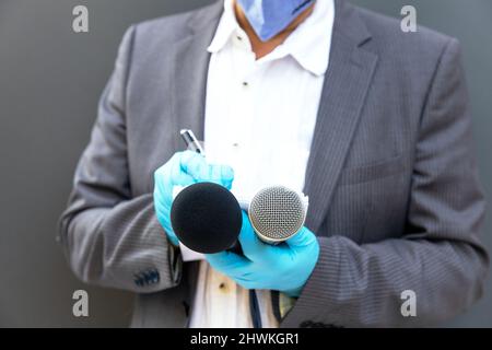 Journalist mit Schutzhandschuhen und Gesichtsmaske gegen COVID-19-Krankheit mit Mikrofon, das während einer Viruspandemie berichtet Stockfoto