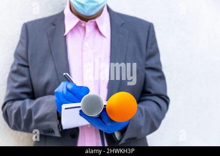 Reporter mit Schutzhandschuhen und Gesichtsmaske gegen COVID-19-Krankheit mit Mikrofon, das während einer Viruspandemie berichtet Stockfoto