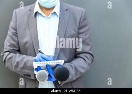 Reporter mit Schutzhandschuhen und Gesichtsmaske gegen COVID-19-Krankheit mit Mikrofon, das während einer Viruspandemie berichtet Stockfoto