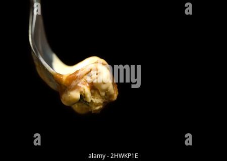 Makrofoto eines Dessertlöffels mit Karamell-Eis vor einem schwarzen Hintergrund mit Kopierfläche. Stockfoto