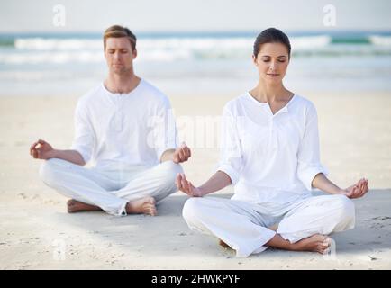 Yoga am Meer. Ein junges Paar, das am Strand Yoga praktiziert. Stockfoto