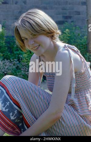 Lächelnde hübsche junge Frau mit blondem bob-Haarschnitt und leichtem Sommerkleid, das Anfang 1980s im Garten-Rugby-england in großbritannien modisch war Stockfoto