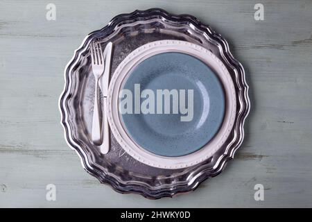 Blauer Teller mit Besteck auf einem glänzenden Metalltablett Stockfoto