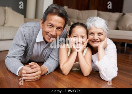 Spaß auf dem Boden mit Oma und Gramps. Ein Mädchen, das sich hinlegt und mit ihren Großeltern lächelt. Stockfoto