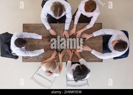 Gruppe von Geschäftsleuten, die Metallgetriebe auf dem Tisch am Arbeitsplatz zusammenbringen, Draufsicht Stockfoto