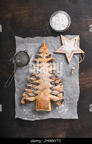 Blätterteig Weihnachtsbaum mit Schokoladenpaste, bestreut mit Puderzucker auf alten dunklen Holzhintergrund. Weihnachts- oder Weihnachtsgebäck. Draufsicht. Co Stockfoto