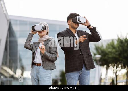 Frontansicht von zwei multiethnischen Geschäftsleuten Freiberufler tragen moderne Brille virtial Realität während der Arbeit gegen außerhalb des modernen Gebäudes Stockfoto