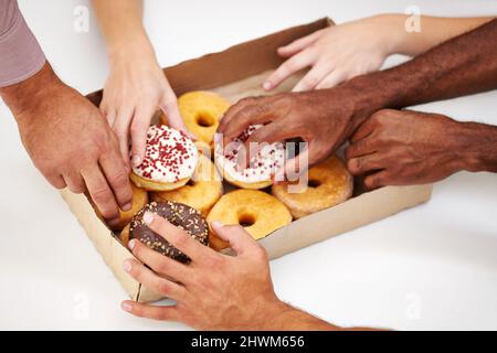 Lassen Sie sich inspirieren. Eine Vielzahl von Händen greifen, um einen Donut aus einer Kiste zu greifen. Stockfoto