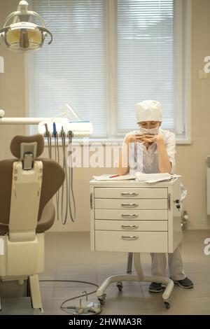 Eine Zahnärztin in ihrem medizinischen Büro, die eine Gesichtsmaske trägt, füllt den Papierkram aus. Stockfoto