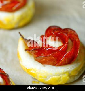 Frisches, hausgemachtes Gebäck. Mischung aus Blätterteig und Vorspeisen. Rosafarbter Pfefferoni-Kuchen. Gebäck mit Salami. Stockfoto