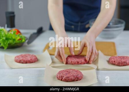 Die Hand einer Frau formt ein Rindfleisch für eine Hamburger-Party. Portionieren von gemahlenem Fleisch. Hausgemachte Burger. Lebensmittel zu Hause machen. Stockfoto