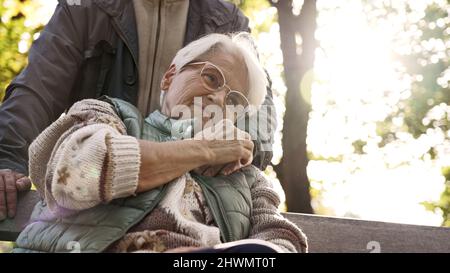 Die ruhige ältere Dame umarmt die Hand ihres pensionierten Mannes, während sie auf einer Bank in einem Park sitzt. Hochwertige Fotos Stockfoto