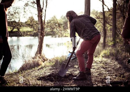 Alternative Person gräbt eine Feuerstelle am Flussufer Stockfoto