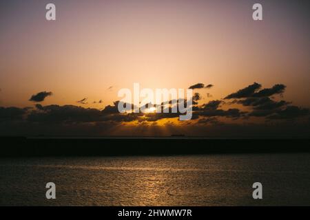 Rosafarbener und orangefarbener Sonnenuntergang mit Sonnenstrahl hinter Wolken Stockfoto