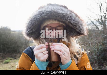 Lächelnde Frau, die sich warm hält und draußen ein heißes Getränk trinkt Stockfoto