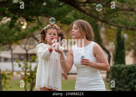 Mutter und Tochter blasen Seifenblasen im Freien. Stockfoto