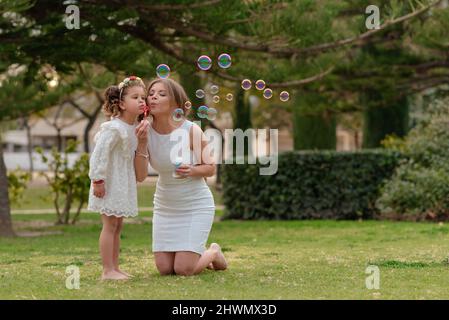 Mutter und Tochter blasen Seifenblasen im Freien. Stockfoto