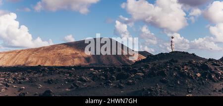 Frau, die sich mit den Händen in den Himmel erhebt und einen atemberaubenden Blick auf die vulkanische Landschaft im Timanfaya-Nationalpark auf Lanzarote, Spanien, genießt. Freiheit und Reisen Stockfoto