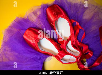 Rote Ballet spitzenschuhe auf einem violetten Tutu und einem gelben Hintergrund. Stockfoto