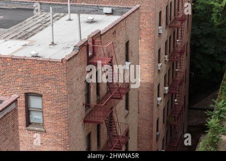 Rückseite von unscheinbaren, generisch aussehenden roten Backsteinhäusern mit Feuertreppen und Fenster-Klimaanlagen Stockfoto