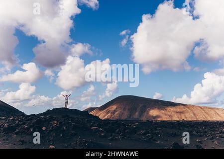 Frau, die sich mit den Händen in den Himmel erhebt und einen atemberaubenden Blick auf die vulkanische Landschaft im Timanfaya-Nationalpark auf Lanzarote, Spanien, genießt. Freiheit und Reisen Stockfoto