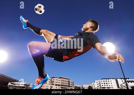 Diese Technik ist einwandfrei. Aufnahme eines jungen Fußballers, der mitten in der Luft einen Ball tritt. Stockfoto