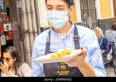 Eine Kellnerin in Gesichtsmaske mit einem Teller Tapas in der modernen Tapas-Bar El Pasaje. Barrio de Santa Cruz, Sevilla, Spanien Stockfoto