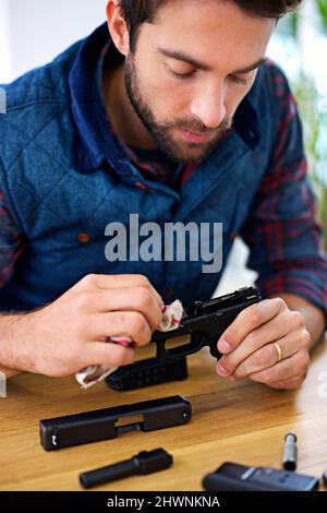 Regelmäßige Wartung ist für jeden Waffenbesitzer unerlässlich. Ein junger Mann, der seine Waffe putzt. Stockfoto