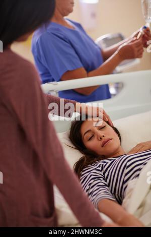 Geht es bald wieder gut Aufnahme einer Frau, die die Stirn ihrer Freunde berührt, während sie in ihrem Krankenhausbett liegt. Stockfoto