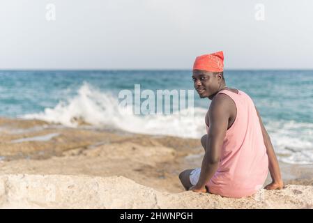 Schwarzer Mann, der auf dem Sand sitzt, mit umgedrehtem Kopf Stockfoto