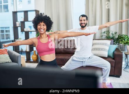 Aus diesem Video haben wir alles gelernt, was wir wissen. Aufnahme eines Paares, das beim Yoga-Üben zu Hause den Fernseher ansah. Stockfoto