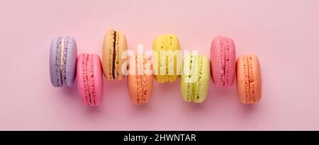 Bunte leckere französische Dessert-Makronen oder Makronen in einer Reihe auf rosa Hintergrund. Draufsicht mit Kopierbereich. Stockfoto