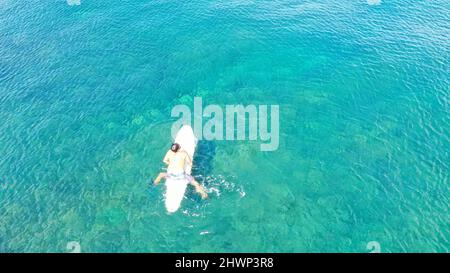 Luftaufnahme des sportlichen jungen Mannes, während sie auf dem Sup Board in türkisfarbenem Wasser reitet. Aufblasbares Sup Board oder Surfboard, Paddle Board Mann auf dem Wasser Stockfoto