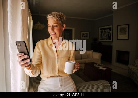 kaukasische ältere Frau, die im Wohnzimmer Selfie nimmt, während sie den Morgenkaffee genießt Stockfoto
