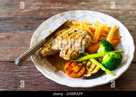 Gebratenes Schweinekotelett, Pommes und Gemüsesalat auf weißem Teller Stockfoto