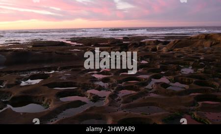 Erodierte Felsformation, Gezeitenbecken in La Jolla, kalifornische Küste, USA. Erosion der Küstenintertidalen Zone, Entlastung der Tidepool. Reflexion des Sonnenuntergangs am Himmel in Wasser, Hohlräumen, Höhlen und Löchern auf der Steinoberfläche Stockfoto