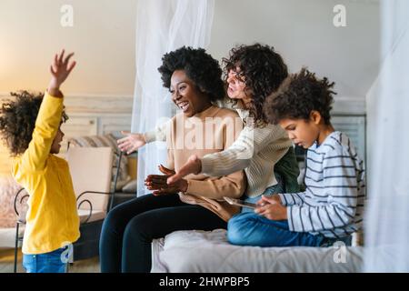 Glückliche multiethnische Familie. Lächelnde schwule Frauen verbringen zu Hause Zeit mit Kindern. Stockfoto