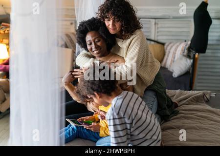 Glückliche multiethnische Familie. Lächelnde schwule Frauen verbringen zu Hause Zeit mit Kindern. Stockfoto