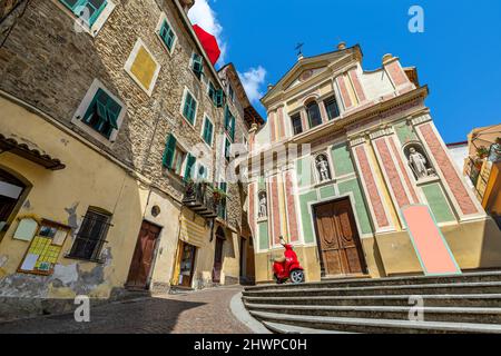 Roter Roller auf dem kleinen Stadtplatz zwischen alten Steinhäusern und katholischer Kirche unter blauem Himmel in Dolceacqua, Ligurien, Italien. Stockfoto