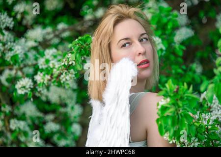 Schöne weibliche Frau mit weißen Flügeln mit weißen Frühlingsblumen. Stockfoto