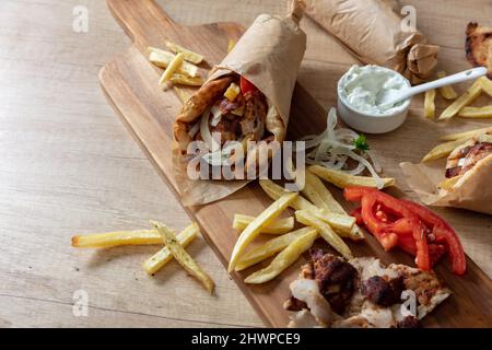 Gyro Pita Shawarma Vorbereitung auf Holztisch, Draufsicht. Griechische Küche, Fleisch in Scheiben, Kartoffeln, Tomaten und Zatziki, Papierverpackung. Stockfoto