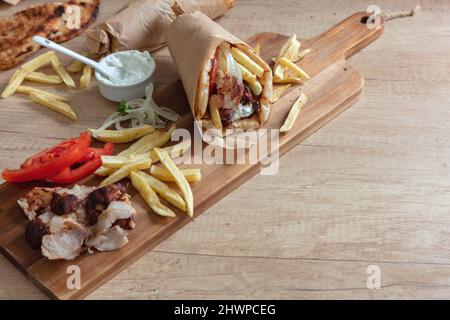 Shawarma Gyro Pita Vorbereitung auf Holztisch, Nahaufnahme. Griechische Küche, Fleisch in Scheiben, Kartoffeln, Tomaten und Zatziki, Papierverpackung. Speicherplatz kopieren Stockfoto