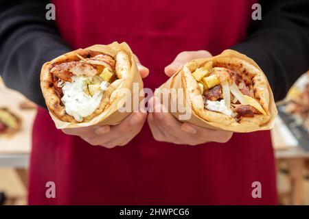 Gyro Pita Shawarma. Griechisches Essen, Fleisch in Scheiben, Kartoffeln, Tomaten und Zatziki, Papierverpackung in männlicher Hand, Nahaufnahme. Stockfoto