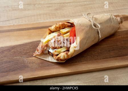 Gyro Pita Shawarma auf Holztisch. Griechische Lebensmittel, Fleisch in Scheiben, Kartoffeln, Tomaten und Zatziki, Papierverpackung, Nahaufnahme. Stockfoto