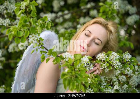 Schöne weibliche Frau mit weißen Flügeln mit weißen Frühlingsblumen. Stockfoto