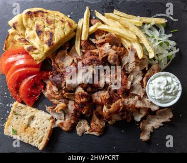 Griechischer Gyro traditionelle Fleischgerichte, ethnische Gerichte, in dünne Scheiben geschnittenes Fleisch, Pita-Brot und Tsatziki-Joghurt auf schwarzem Hintergrund, Draufsicht. Stockfoto
