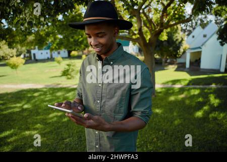Gemischter Rassenbauer, der auf einem digitalen Tablet im Freien steht, tippt Stockfoto