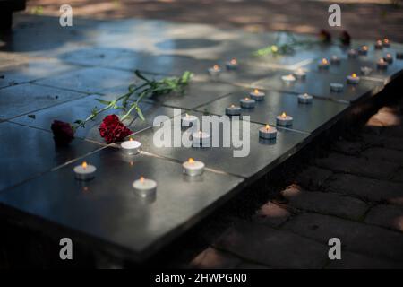 Kerzen auf Grabstein. Wachskerzen brennen auf dem Kriegsdenkmal. Zwei Blumen auf Grabstein. Begräbnisstätte der Soldaten. Memorial Complex im Detail. Stockfoto